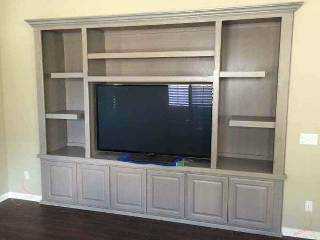 Built-in gray entertainment center with TV, shelves, and cabinets against a beige wall.