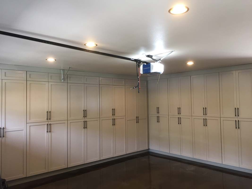 Garage with white storage cabinets on two walls, overhead door track, and ceiling lights.