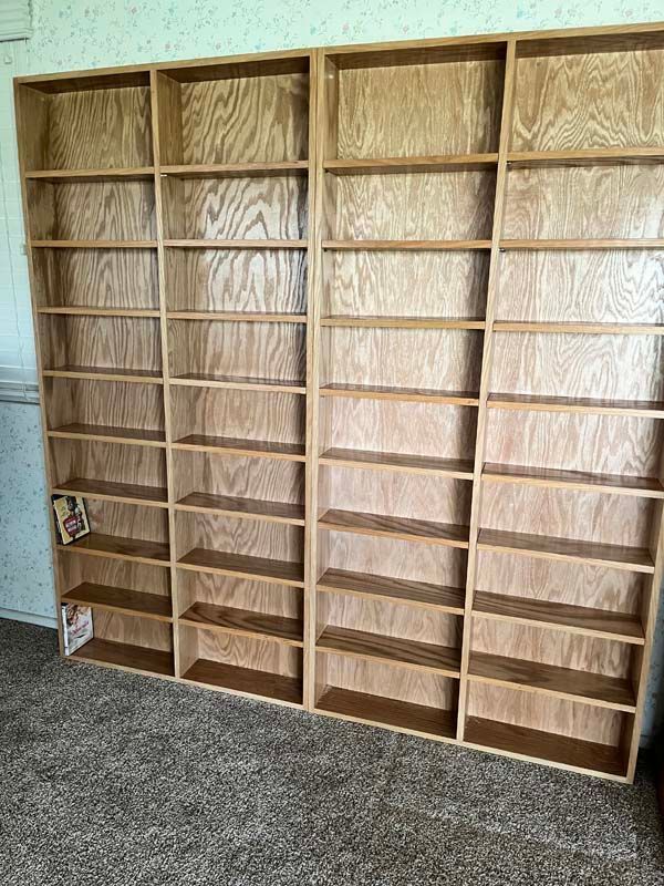 Large, empty wooden bookshelf against a wall on a patterned carpet.