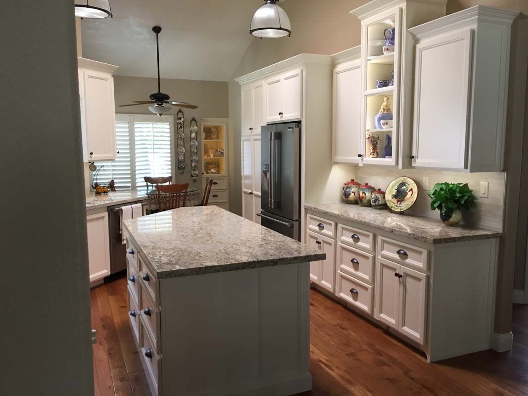White kitchen with island, cabinets, refrigerator, and wood floor. Granite countertops.