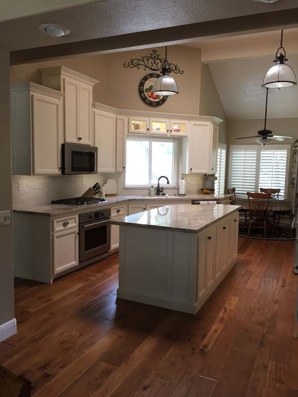 Bright white kitchen with island, white cabinets, stainless appliances, hardwood floor.