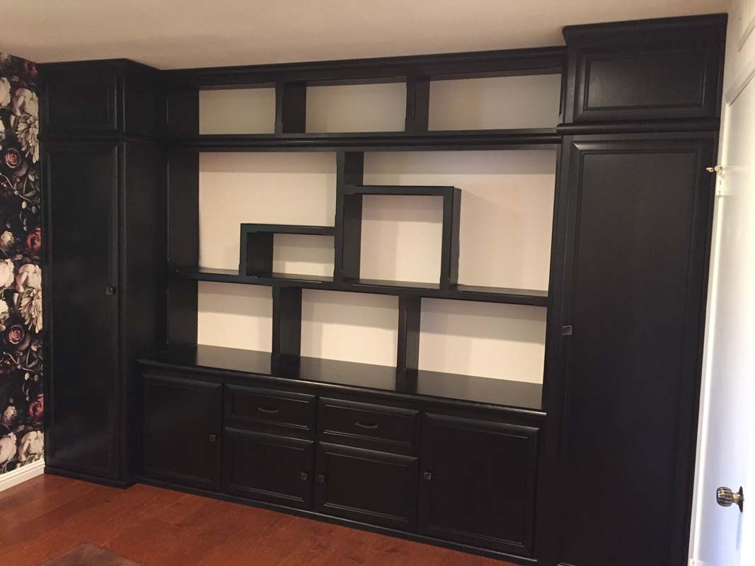 Black built-in entertainment center with shelves and cabinets against a white wall.