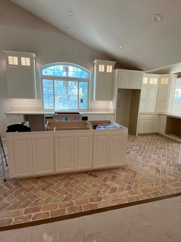 Kitchen under construction with cream cabinets, brick floor, arched window.