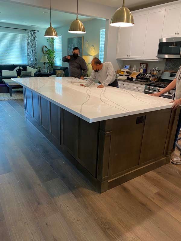 Three people installing a white countertop on a large kitchen island with a brown cabinet base.