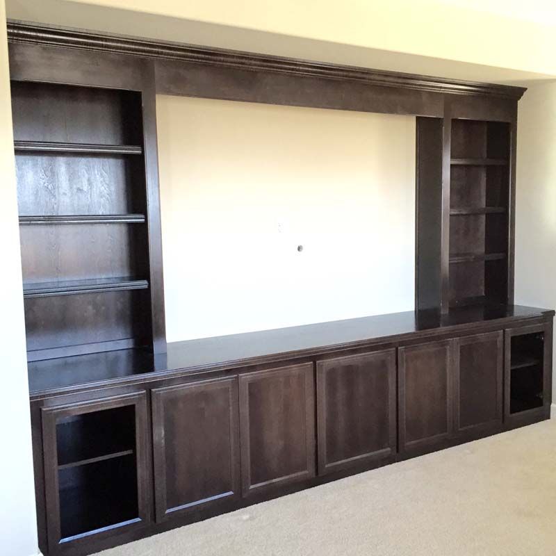 Built-in dark brown entertainment center with shelves and cabinets on a beige carpet.