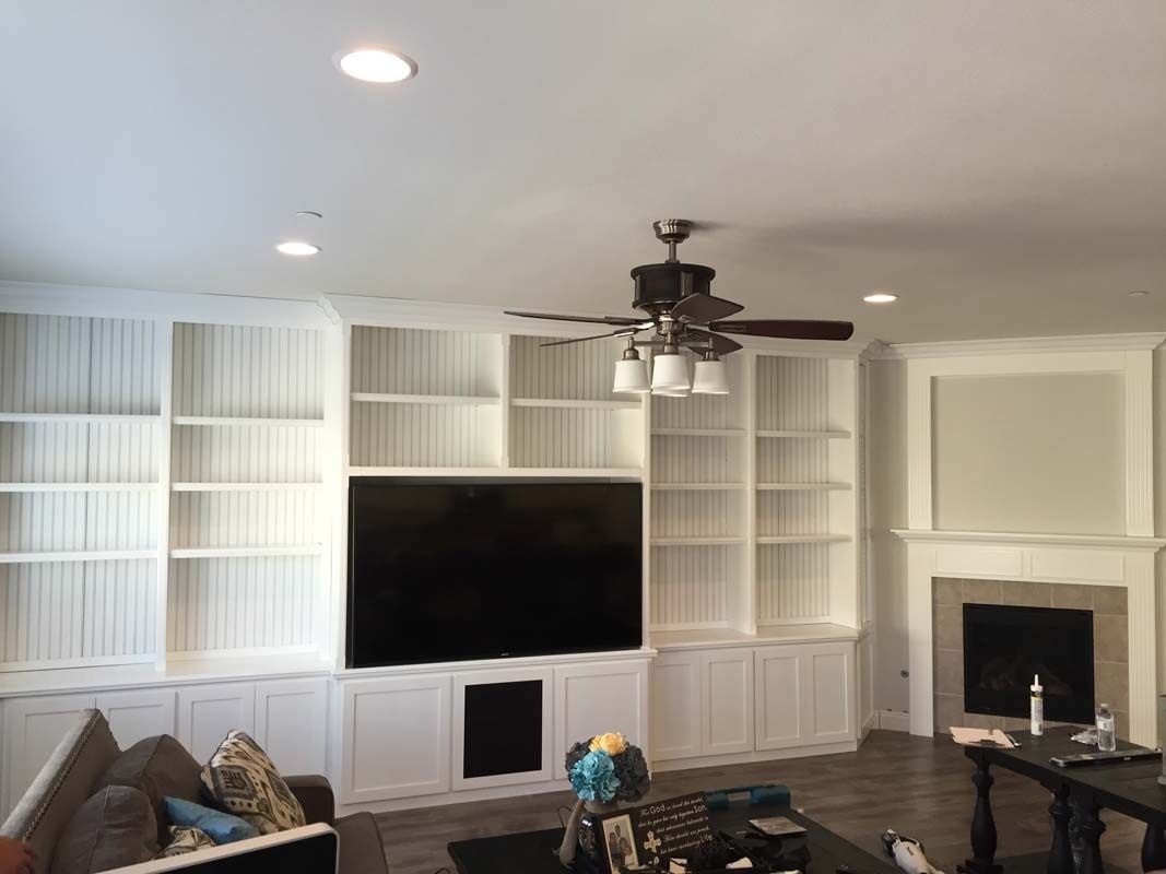 Living room with white built-in bookshelves, a large TV, and a fireplace. A ceiling fan hangs above.