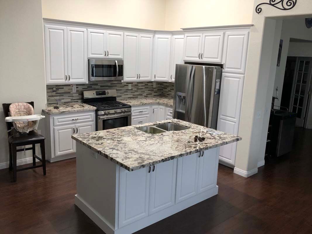 White kitchen cabinets and island with stainless steel appliances and granite countertops.