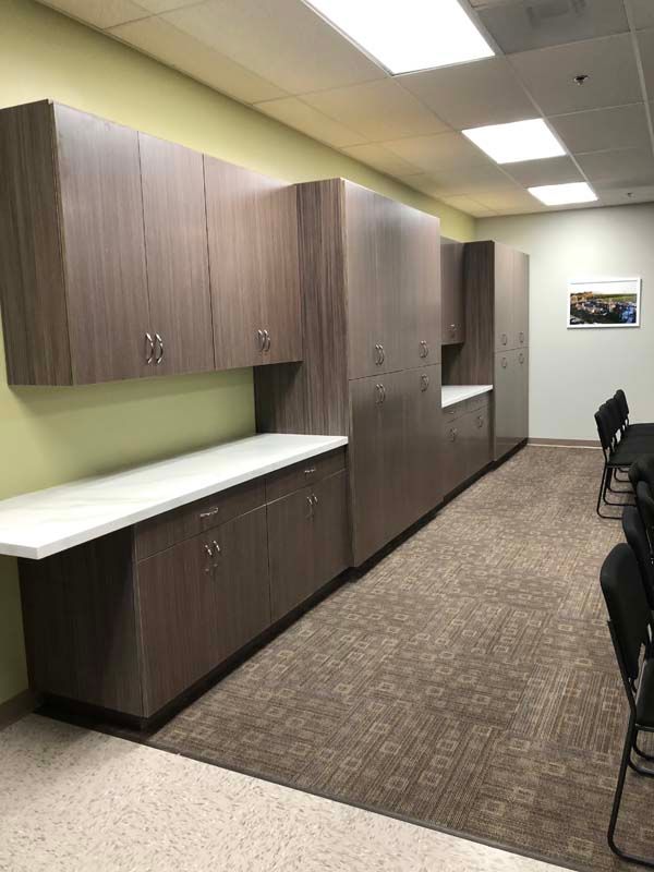 Built-in wood cabinets and countertops line a room with a brown carpet and chairs.