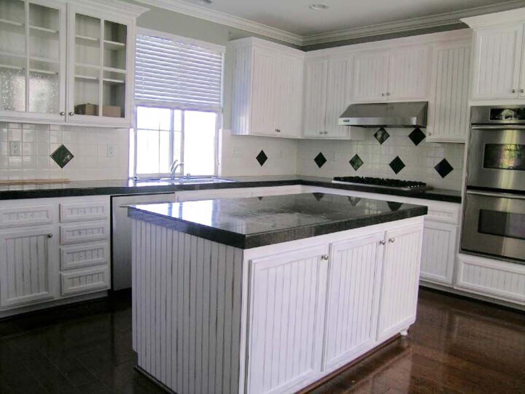 White kitchen with black countertops and island, stainless steel appliances, and wood floors.