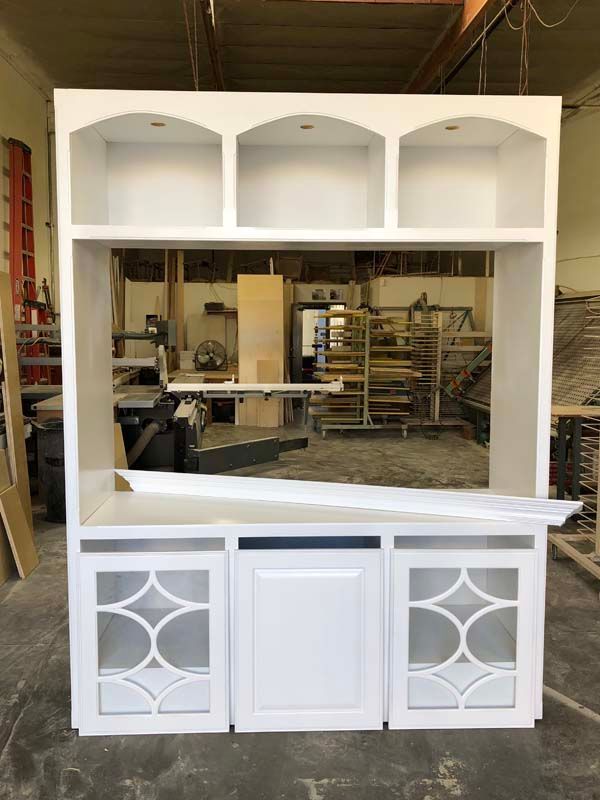 White built-in cabinet with arched shelves, open center space, and glass-paneled doors. Workshop setting.
