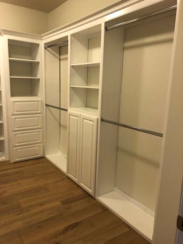 White custom closet with shelves, drawers, and hanging rods. Hardwood floor.