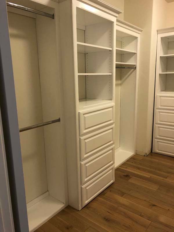 White custom closet with shelves, drawers, and hanging rods; set in a room with wood flooring.