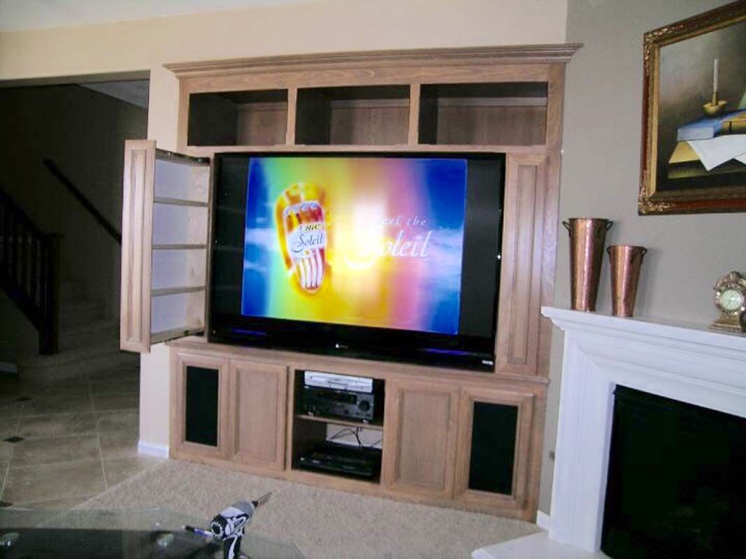 Built-in wooden entertainment center with TV playing colorful images, speakers, and shelves. A fireplace is visible.