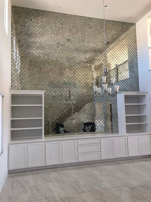 Built-in white cabinets with bookshelves, a decorative tile wall, and a staircase. A chandelier hangs in a spacious room.