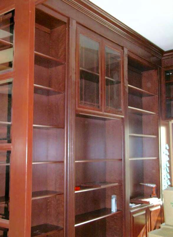 Built-in wooden bookshelves, stained dark red, with glass-fronted cabinets in the center.
