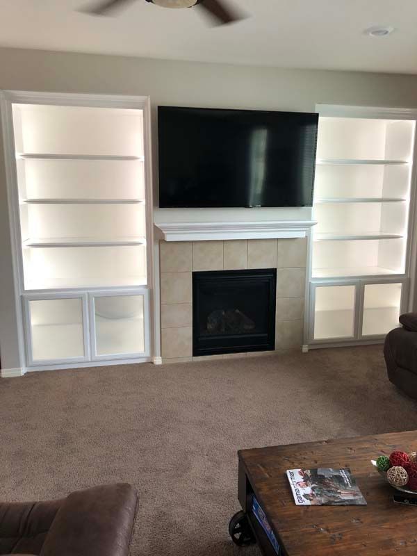 Built-in white bookshelves on either side of a fireplace with a mounted TV above it. Brown carpet.