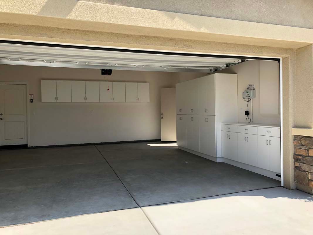 Open, empty garage with white cabinets and gray concrete floor.