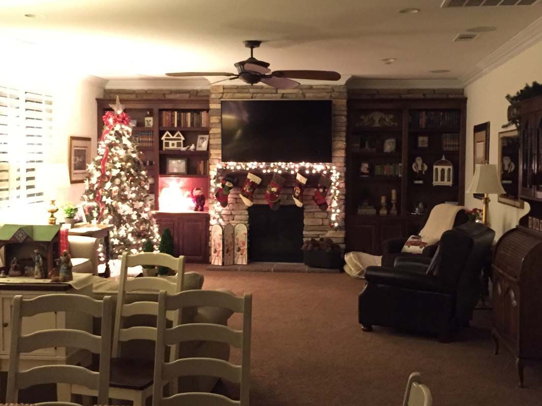 Christmas-decorated living room with tree, fireplace, built-in shelves, and dining table.