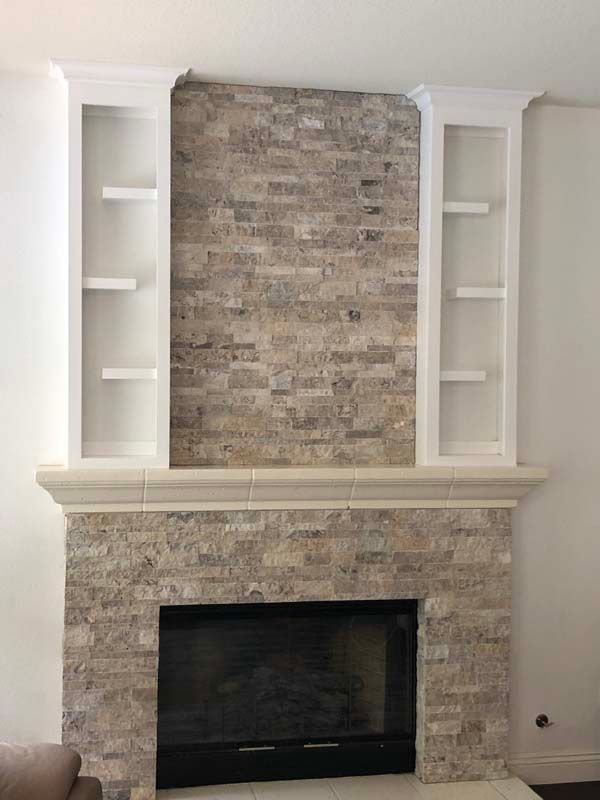Fireplace with stacked stone facing, flanked by white bookshelves.