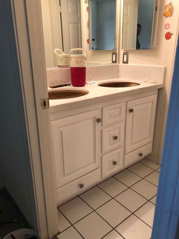 White bathroom vanity with two sinks, two mirrors, and white tile floor.