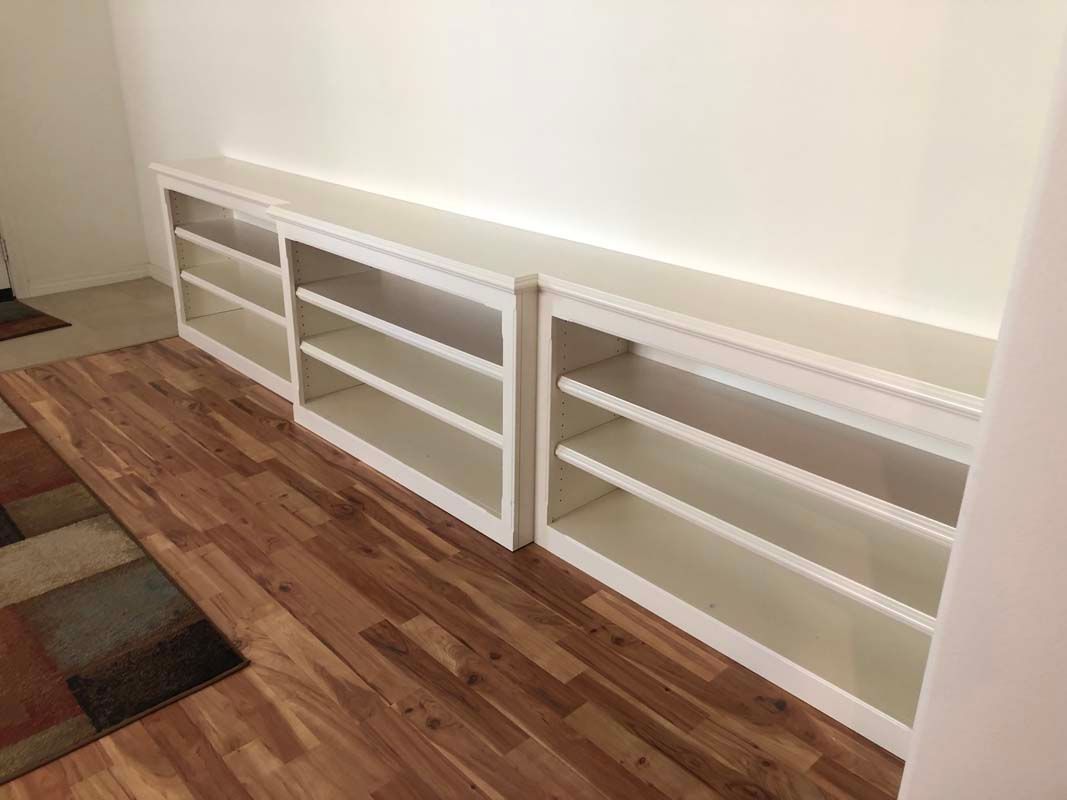 Built-in white bookshelves on a wood floor against a white wall. Three sections with three shelves each.