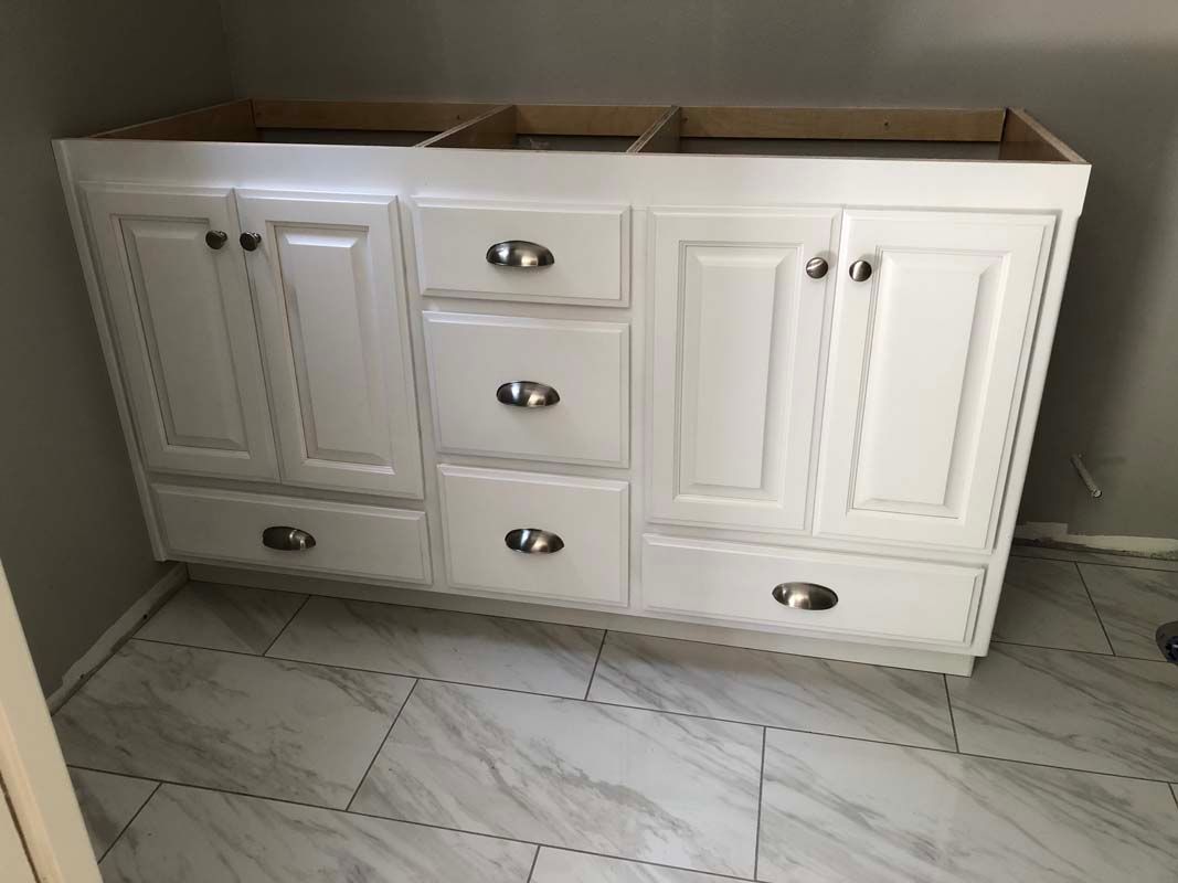 White bathroom vanity cabinet with drawers and doors; sits on a tiled floor.