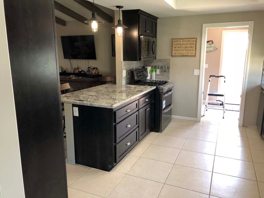 Dark-cabinet kitchen with island, granite countertop, and tile floor, with an open doorway to a hallway.