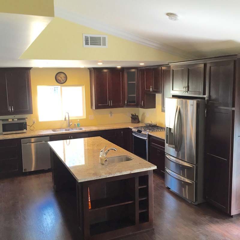 Kitchen with dark cabinets, stainless steel appliances, island, and yellow walls.