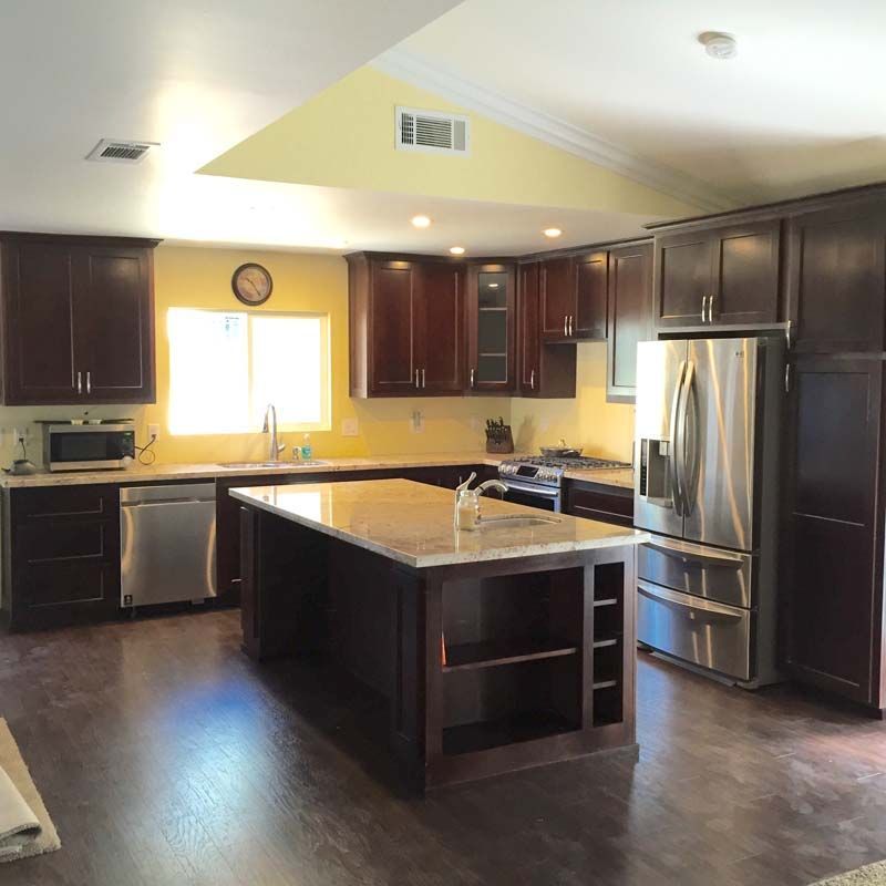 Kitchen with dark wood cabinets, stainless steel appliances, island, and yellow walls.