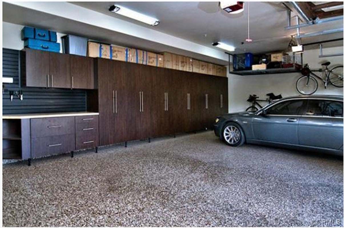 Organized garage with dark wood cabinets, car, bikes, and storage. Gray speckled floor.