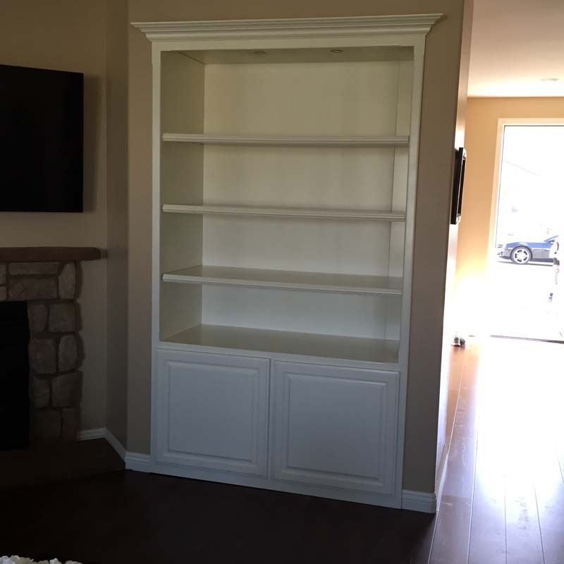 White built-in bookshelf with shelves above two cabinet doors, installed on a tan wall.
