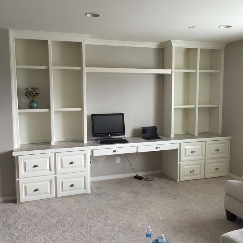 Built-in white desk and bookshelves with a computer and laptop on a light carpet.