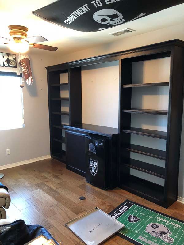 Room with wooden built-in shelves, a black safe with Raiders logo, and Raiders flag on the ceiling.