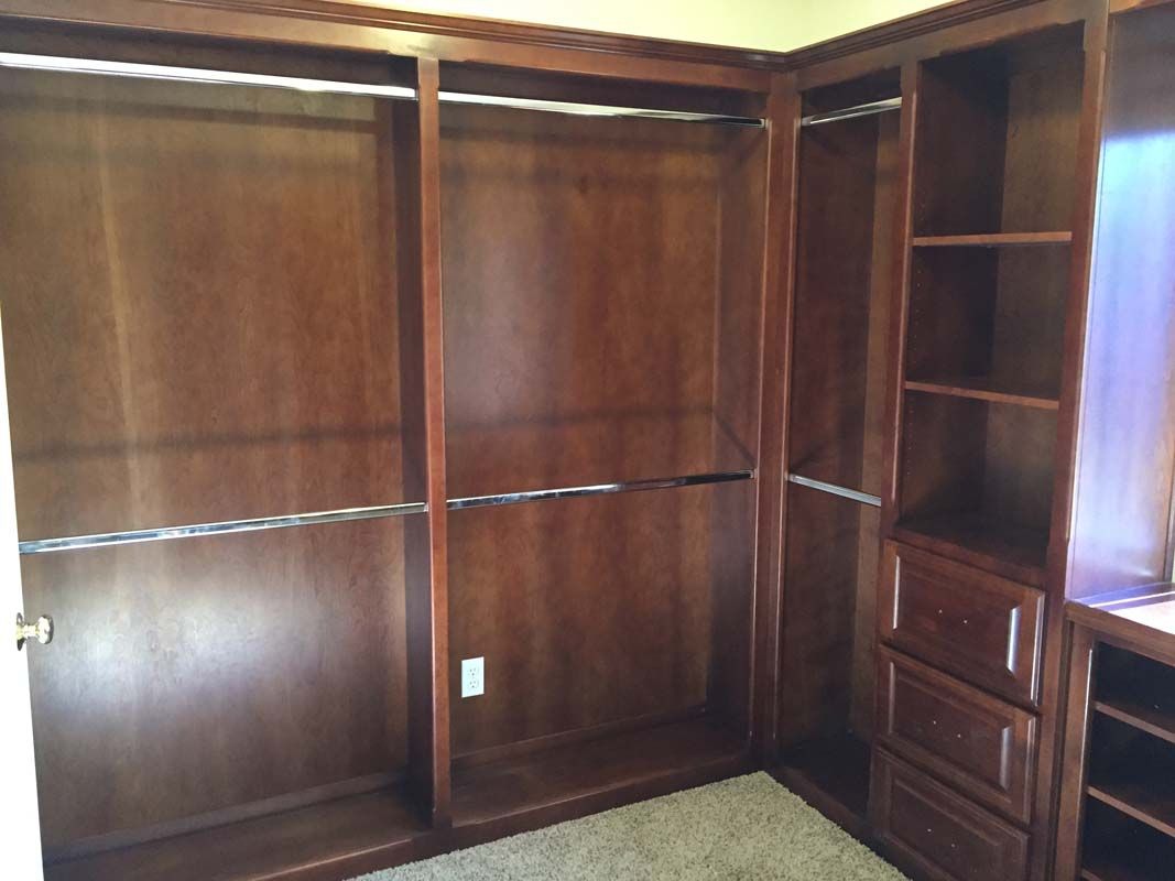 Empty, dark wood closet with shelves, drawers, and hanging rods. Carpet on floor.