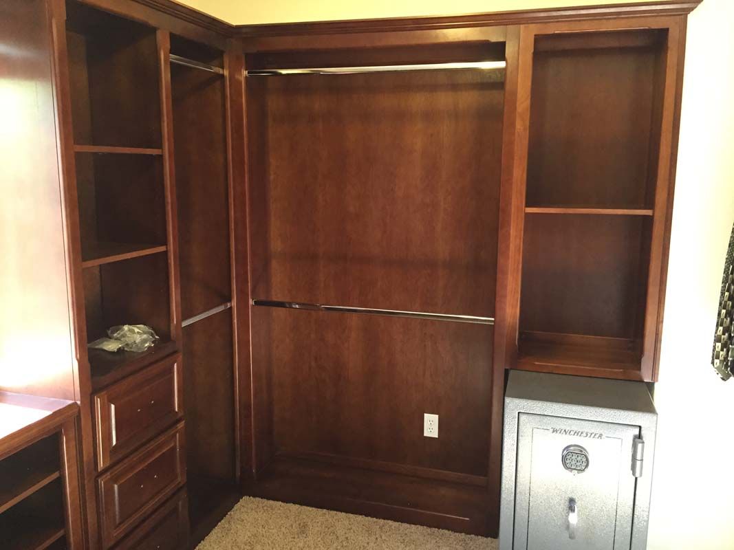 Built-in dark wood closet with shelves, drawers, and a safe on a carpeted floor.