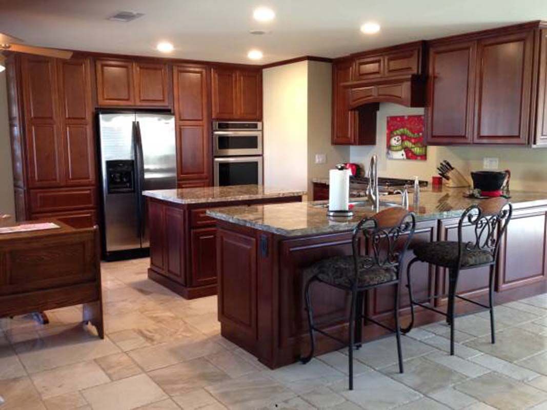 A kitchen with dark wood cabinets, granite countertops, and two islands.
