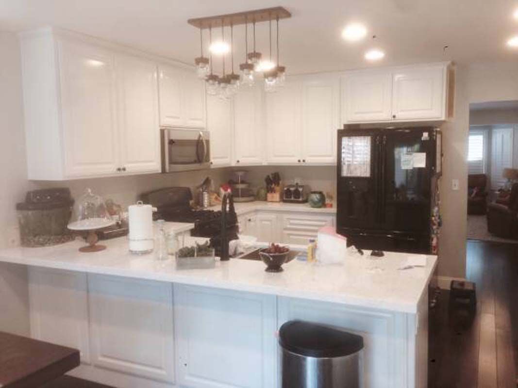 White kitchen with white cabinets, marble countertop, and black refrigerator.