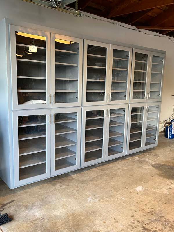 Gray glass-front cabinets with multiple shelves, mounted on a concrete floor in a garage.