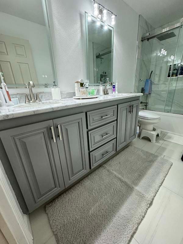 Gray bathroom vanity with marble countertop, mirror, and a gray rug in front.
