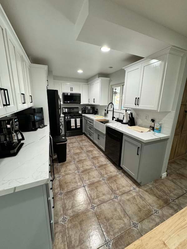 Kitchen with white upper cabinets, gray lower cabinets, black appliances, and patterned tile floor.