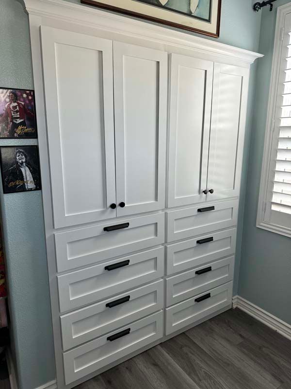 White built-in cabinet with six drawers and four doors; black hardware against a blue wall and wood floor.