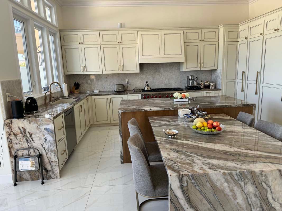 Bright kitchen with cream cabinets, marble countertops, two islands, and large windows.