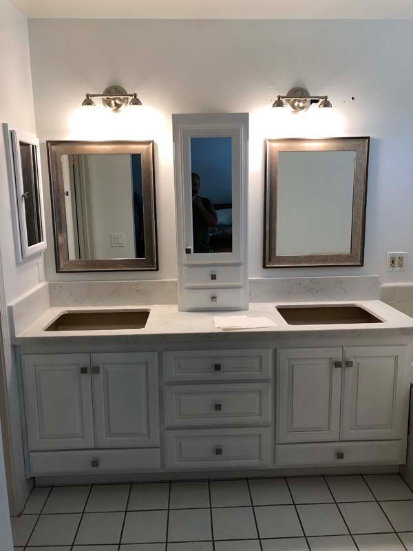 Double vanity with white cabinets, light countertop, three mirrors, and sconces.