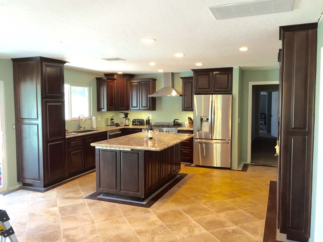 Kitchen with dark cabinets, island, stainless steel appliances, and tile floor.