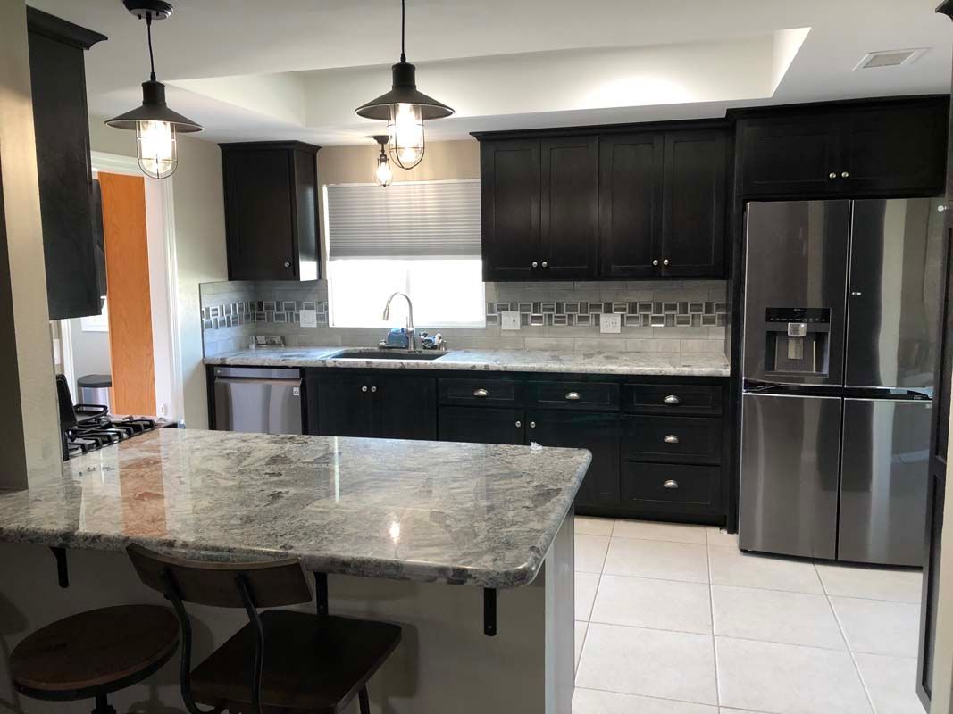 Dark kitchen with stainless steel appliances, granite countertops, and two pendant lights.