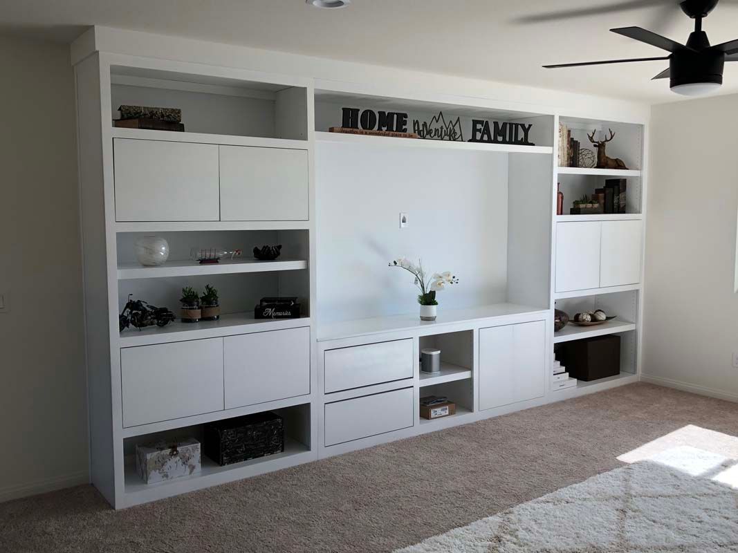 White built-in shelving unit with cabinets and open shelves on a beige carpeted floor.