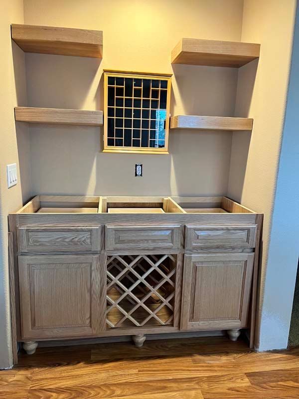 Unfinished wooden bar area with shelves above cabinets, a wine rack, and a decorative square.