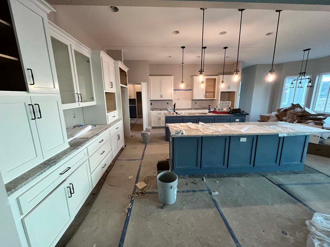 Kitchen renovation: White cabinets, blue island, pendant lights. Construction materials on the floor.