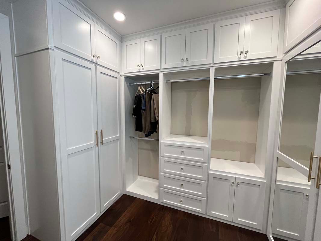 White walk-in closet with built-in storage, drawers, and hanging rods. Dark wood floor.
