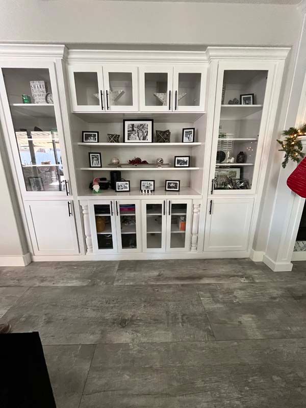 White built-in cabinet with glass doors, displaying photos and decorative items on shelves.
